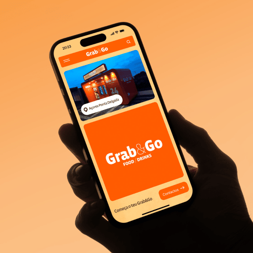 Hand holding a smartphone displaying the Grab&Go app interface. The app screen features an image of a Grab&Go vending machine in Ponta Delgada, with a bright orange and white branding theme. The screen includes navigation options and buttons, creating a vibrant, user-friendly experience on a gradient orange background.